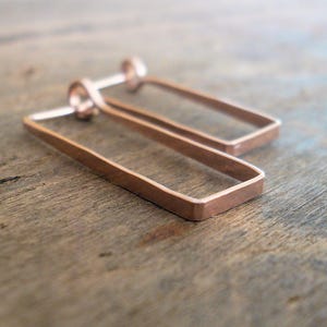 May include: A pair of rose gold earrings with a rectangular shape. The earrings are made of thin metal and have a simple, modern design.