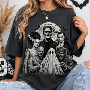 Peut inclure: Un t-shirt gris anthracite orné d'une impression graphique représentant des monstres classiques de films d'horreur, dont le monstre de Frankenstein, la fiancée de Frankenstein, Dracula, une momie, un loup-garou et un fantôme devant une pleine lune.