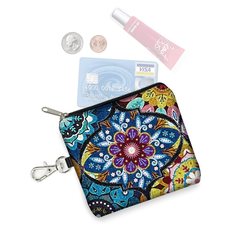 May include: A small, colorful zippered pouch with a mandala design. The pouch has a black zipper and a silver key ring attached. A credit card with the text "VISA" and a tube of lip balm are visible inside the pouch.