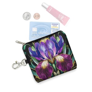May include: A small black zippered coin purse with a vibrant purple iris flower design. The purse has a silver clasp and a key ring attachment. A Visa credit card, lip gloss, and coins are also visible.