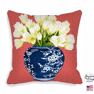 Pode incluir: Um arranjo floral branco de tulipas em um vaso de porcelana azul e branco com um design floral. O vaso está sobre um fundo vermelho com um padrão geométrico.