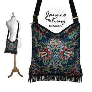 Puede incluir: Un bolso bandolera negro con un dise&ntilde;o de tapicer&iacute;a floral y flecos negros. El bolso tiene una cremallera dorada y una correa ajustable negra. El bolso est&aacute; hecho por Janine King Designs.
