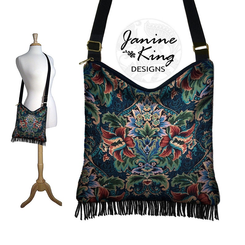 Puede incluir: Un bolso bandolera negro con un dise&ntilde;o de tapicer&iacute;a floral y flecos negros. El bolso tiene una cremallera dorada y una correa ajustable negra. El bolso est&aacute; hecho por Janine King Designs.