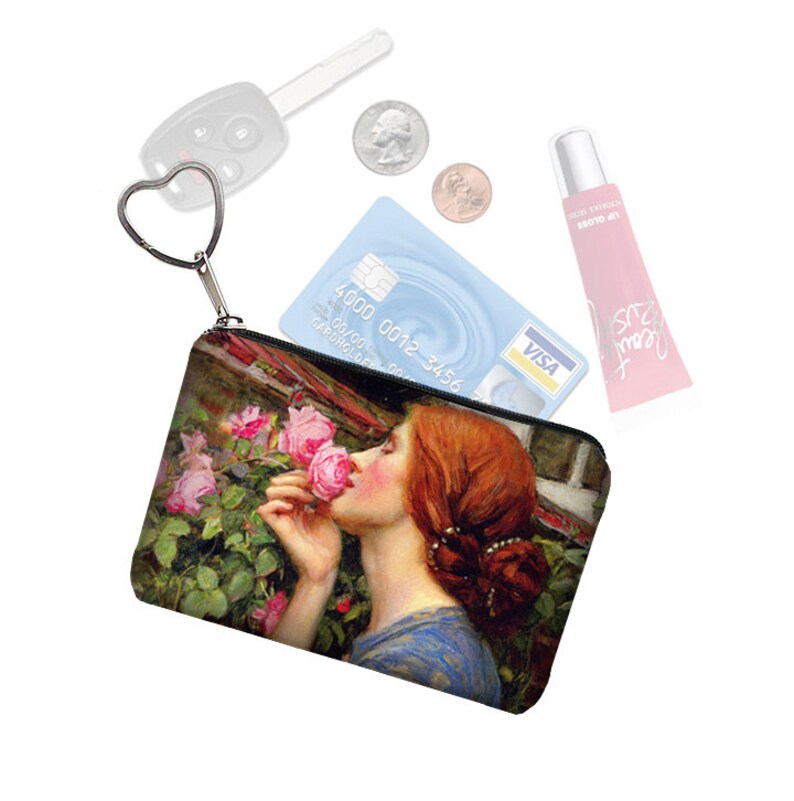 K&ouml;nnte beinhalten: Eine kleine schwarze Rei&szlig;verschlusstasche mit einem Blumendruck, der eine Frau zeigt, die an einer rosa Rose riecht. Die Tasche hat einen silbernen herzf&ouml;rmigen Schl&uuml;sselanh&auml;nger.