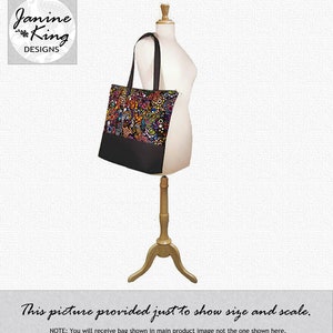 Puede incluir: Una bolsa tote negra con un estampado floral colorido y cierre de cremallera. La bolsa est&aacute; en un maniqu&iacute; de madera. "Esta imagen se proporciona solo para mostrar el tama&ntilde;o y la escala. AVISO: Recibir&aacute; la bolsa que se muestra en la imagen principal del producto, no la que se muestra aqu&iacute;."