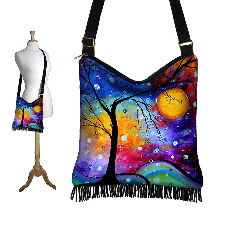 May include: A colorful abstract painting of a tree with a large yellow moon in the background. The painting is printed on a black canvas tote bag with a fringe trim.