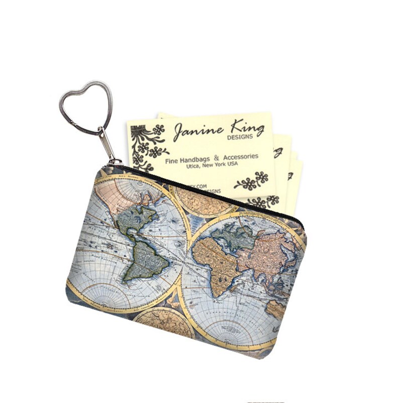 May include: A small zippered pouch with a heart-shaped keychain. The pouch is printed with a vintage world map design in shades of blue, brown, and yellow. The pouch is partially open, revealing a stack of business cards with the text "Janine King Designs Fine Handbags & Accessories Utica, New York USA" printed on them.