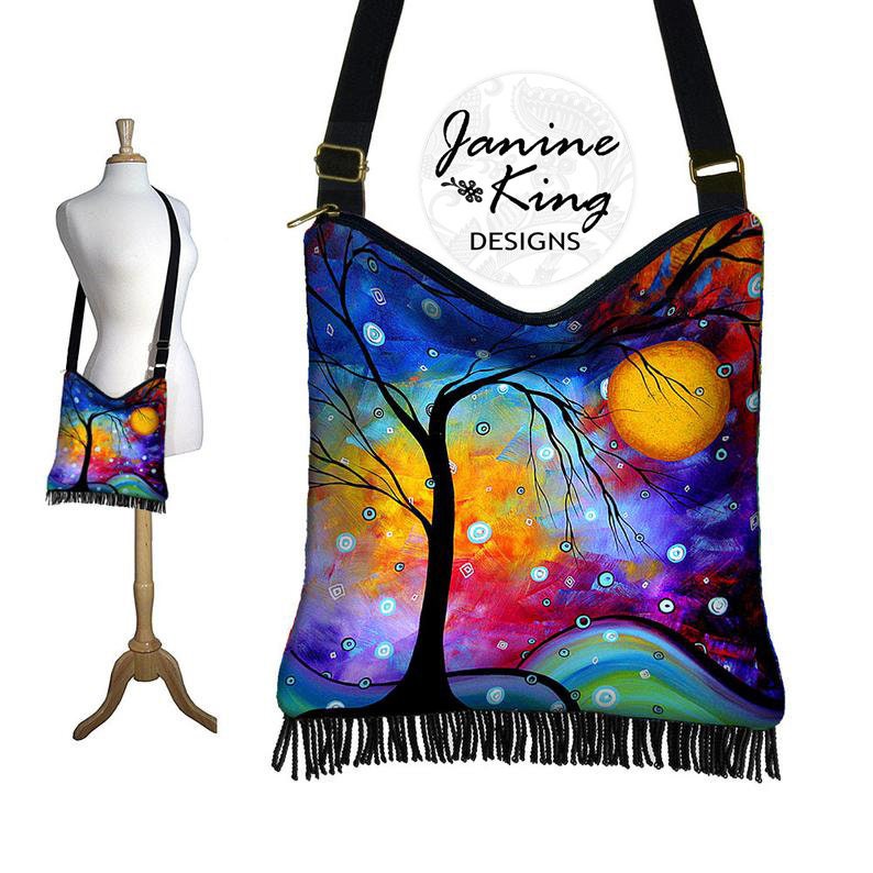 May include: A colorful, abstract painting of a tree with a large yellow moon in the background. The painting is on a black canvas bag with a fringe trim. The bag has a long strap and is perfect for carrying everyday essentials.
