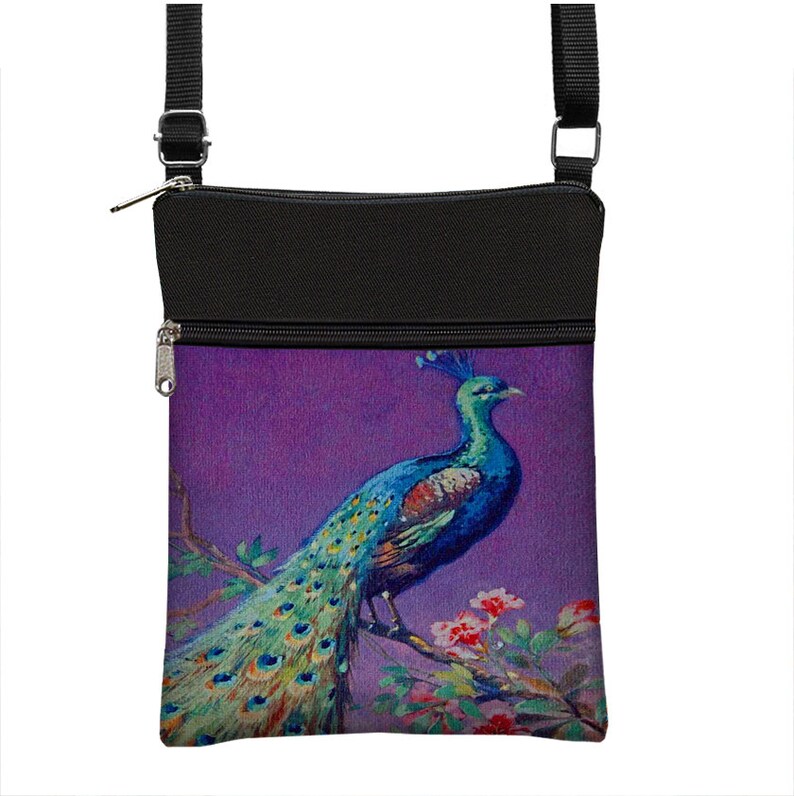 Pode incluir: Uma bolsa de ombro de lona preta com fecho de correr. A frente da bolsa apresenta uma pintura colorida de um pav&atilde;o com as suas penas da cauda espalhadas sobre um fundo roxo.