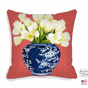 Pode incluir: Almofada quadrada com um design em aquarela. Apresenta um vaso azul e branco cheio de tulipas brancas sobre um fundo vermelho padronizado. A almofada tem o texto "Janine King Designs" e "Made in USA".
