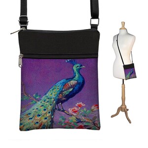 Pode incluir: Uma bolsa de ombro preta com fundo roxo e uma ilustra&ccedil;&atilde;o colorida de pav&atilde;o. A bolsa tem fecho de correr e uma al&ccedil;a longa ajust&aacute;vel.