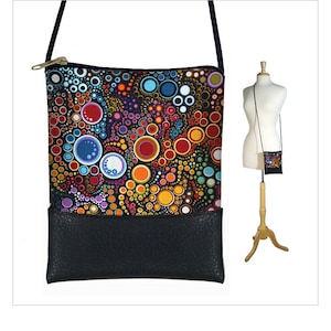 May include: A black crossbody bag with a colorful circle pattern and a black leather bottom. The bag has a zipper closure and a long adjustable strap.