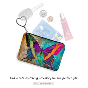May include: A small zippered pouch with a colorful butterfly design. The pouch is made of fabric and has a heart-shaped zipper pull. The pouch is open and contains a credit card, a key, and a tube of lip gloss.