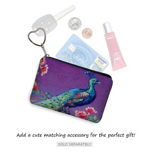 Pode incluir: Uma pequena bolsa roxa com z&iacute;per e um design de pav&atilde;o. A bolsa est&aacute; aberta e cont&eacute;m um cart&atilde;o de cr&eacute;dito, uma chave e um tubo de brilho labial.