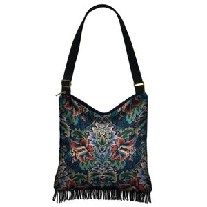 Puede incluir: Un bolso bandolera de estilo tapiz azul oscuro y verde con ribete de flecos. El bolso tiene una correa negra y herrajes dorados.