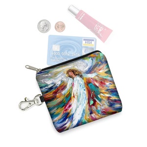 May include: A small zippered pouch with a colorful painting of an angel with outstretched wings. The pouch has a black zipper and a silver key chain attached. The pouch is lying on a white surface with a credit card, two coins, and a tube of lip balm.