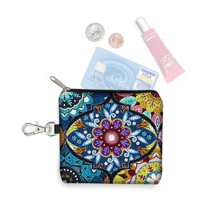 May include: A small zippered pouch with a colorful mandala design. The pouch has a silver zipper and a silver clip. The pouch is open and a credit card with the Visa logo is visible inside. The credit card number is 4000 0012 3456. There are also two coins and a tube of lip balm visible.