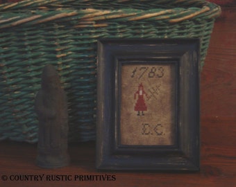 Puede incluir: Un sampler de punto de cruz enmarcado con una mujer con un vestido rojo sosteniendo una escoba. El sampler está fechado en 1783 y firmado "E.C."