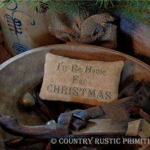 May include: A rustic wooden bowl filled with antique tools and a small pillow with the text "I'll Be Home For Christmas" embroidered on it.