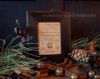 Puede incluir: Un sampler de punto de cruz enmarcado con una escena navideña, que presenta un pequeño carro rojo tirado por un caballo, un árbol y el texto "MH Christmas 1807". El sampler está rodeado por un marco de madera oscura y se muestra sobre una superficie de madera con ramas de pino, una piña y campanas.