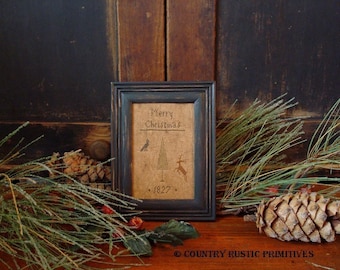 May include: A framed cross-stitch sampler with a black frame and a burlap background. The sampler features a stylized Christmas tree with a bird, a deer, and the text "Merry Christmas 1827".