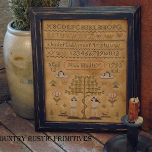 May include: A framed cross-stitch sampler with a black frame. The sampler features a tree with two figures standing beneath it. The sampler also includes a banner with the text "Mun Madley 1793 a.d."