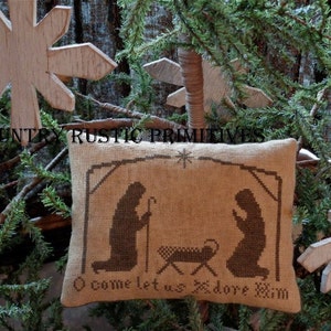 Pode incluir: Uma almofada de juta marrom com um design de ponto cruz que representa a cena da natividade. A almofada tem o texto "O come let us adore Him".