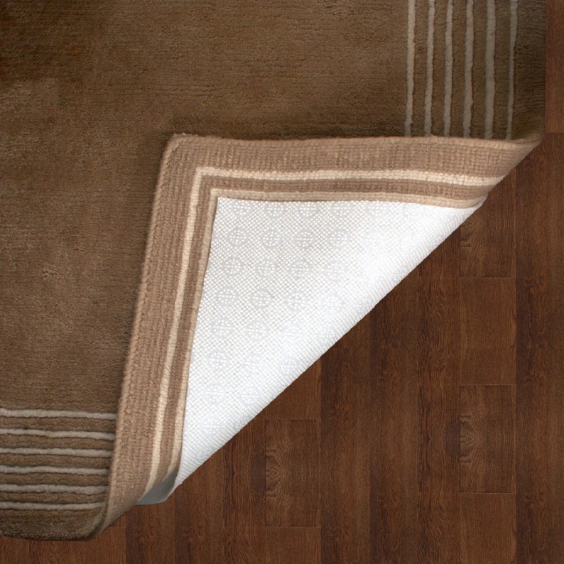 May include: A brown rug with a white border and a white backing. The rug is folded over to show the backing.