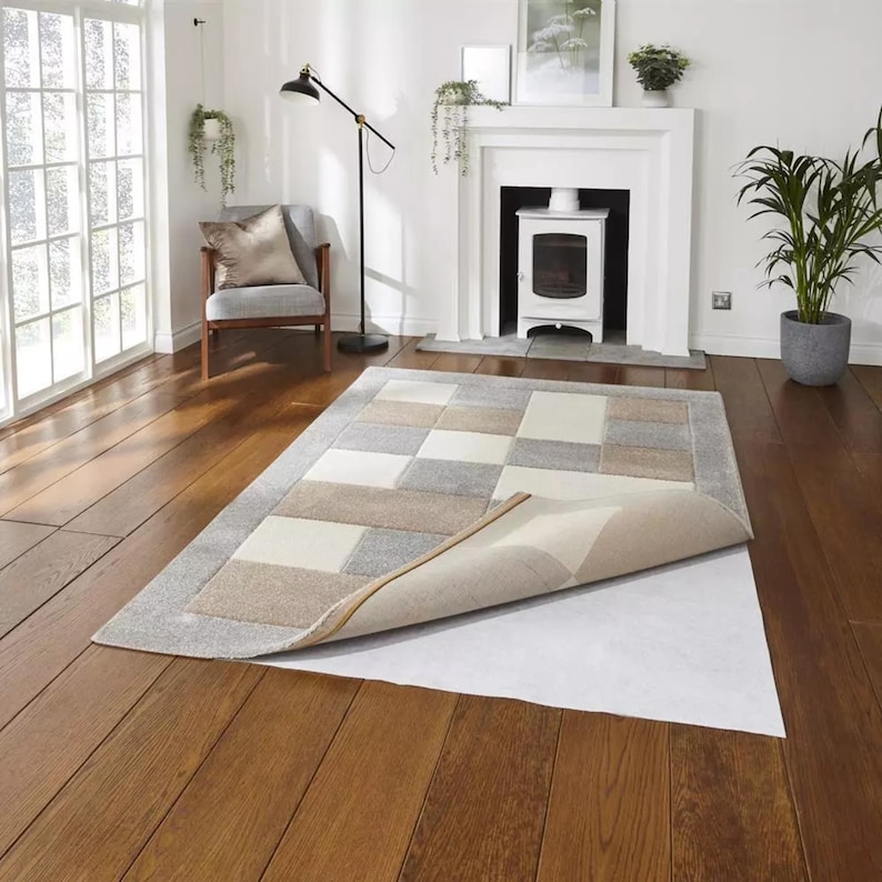 May include: A white rug pad with a beige and gray rug partially rolled up on top of it. The rug has a checkered pattern.