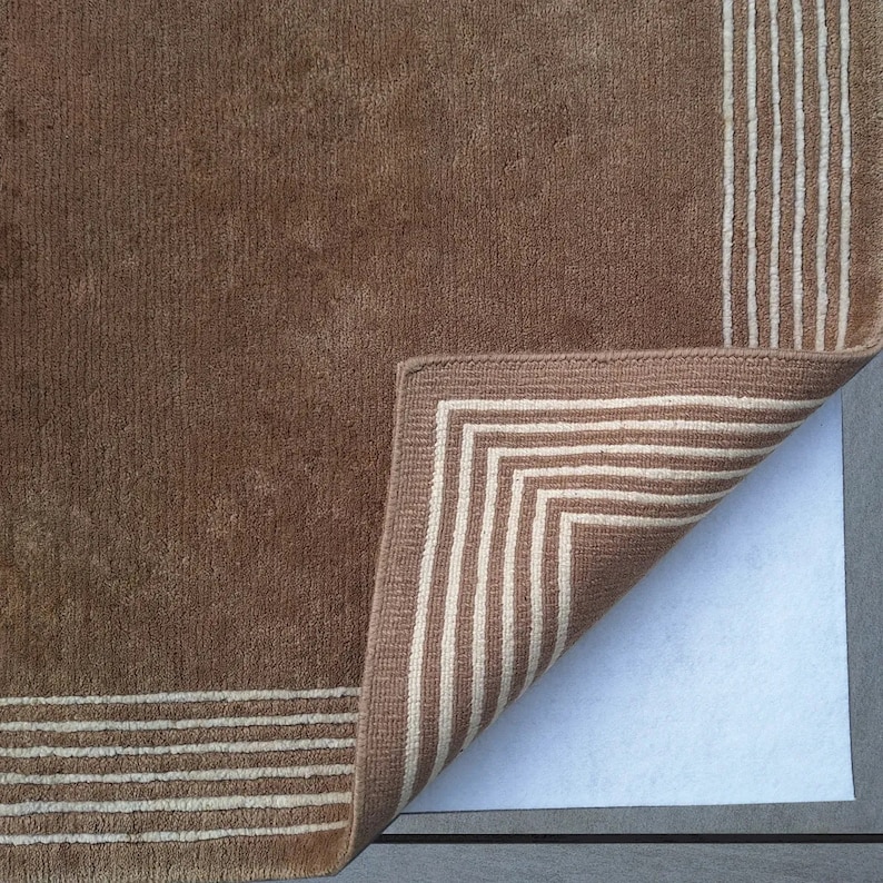 May include: A brown rug with a white border. The rug is folded over to show the underside, which is a white non-slip backing.
