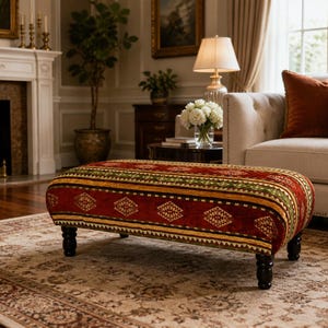 Puede incluir: Un otom&aacute;n tapizado con un dise&ntilde;o estampado en rojo, verde y dorado. El otom&aacute;n rectangular tiene patas de madera oscura y est&aacute; colocado sobre una alfombra estampada. La habitaci&oacute;n cuenta con chimenea, sof&aacute; y l&aacute;mpara. El otom&aacute;n mide unos 120 cm de largo.