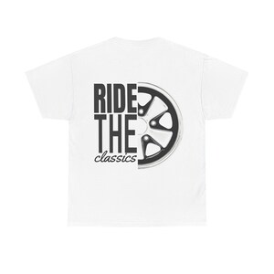 Può includere: T-shirt bianca con la scritta "RIDE THE classics" in nero e una grafica stilizzata di una ruota di moto nera e argento. La maglietta è a girocollo.