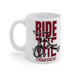 Può includere: Tazza in ceramica bianca con un'illustrazione in bianco e nero di un triciclo. La scritta "RIDE THE classics" è in bordeaux. La tazza ha un manico bianco e un interno bianco.