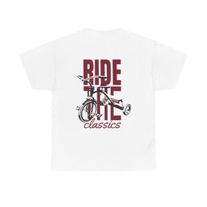 Può includere: T-shirt bianca con grafica bordeaux di un triciclo e le parole "RIDE THE classics". Il disegno è centrato sulla maglietta, con il testo impilato verticalmente.