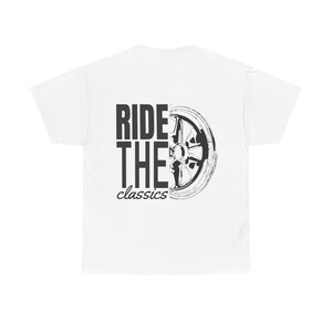 Può includere: T-shirt bianco con la scritta "RIDE THE classics" in nero. Una grafica in bianco e nero di una ruota di auto è a destra del testo. La maglietta è realizzata in un materiale morbido e confortevole.