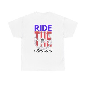 Puede incluir: Camiseta blanca con un diseño gráfico que presenta las palabras "RIDE THE classics" en azul y negro, con un volante en el centro. El diseño está centrado en la parte posterior de la camiseta.