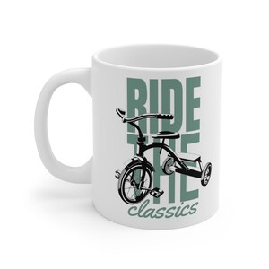Può includere: Tazza in ceramica bianca con un'illustrazione in bianco e nero di un triciclo classico. La tazza presenta le parole "RIDE THE classics" in verde e nero, un design nostalgico.