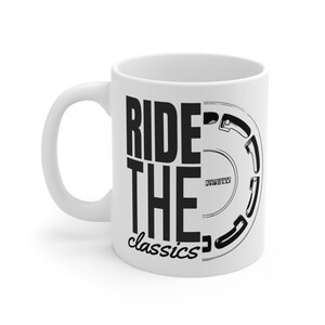 Può includere: Tazza in ceramica bianca con la scritta nera "RIDE THE classics". Il lato destro presenta una grafica in bianco e nero di uno pneumatico con il logo Pirelli.