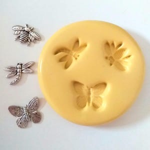 May include: A yellow silicone mould with insect impressions and three silver-coloured metal charms. The mould has dragonfly, butterfly, and bee designs. The charms include a dragonfly, a bee, and a butterfly.