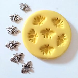 May include: A yellow silicone mould with six bee-shaped impressions and several silver-coloured bee charms. The mould is round, and the bee charms are detailed with wings and body segments. Suitable for crafting or jewellery making.