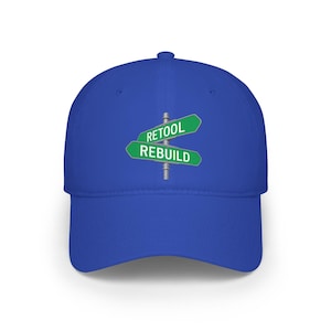 May include: A royal blue baseball cap with a curved brim. The cap features a graphic of a street sign with the words "RETOOL" and "REBUILD" on green signs. The cap is made of a soft material and has a structured crown.