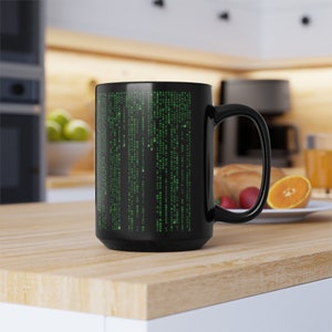 May include: Black coffee mug featuring a green matrix code design. The mug is on a wooden surface.