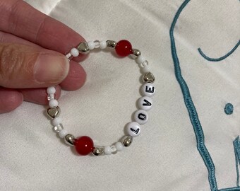 May include: A white and red beaded bracelet with silver heart beads and letter beads spelling out the word "LOVE".