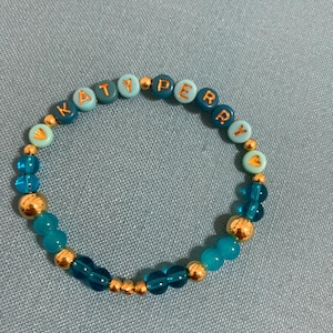May include: A blue and gold beaded bracelet with the name "KATY PERRY" spelled out in gold letters.