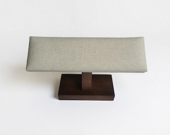 May include: A rectangular jewelry display stand. The base is a dark brown square, supporting a vertical post that holds a long, rectangular, light gray fabric-covered top. The stand is designed to showcase jewelry.