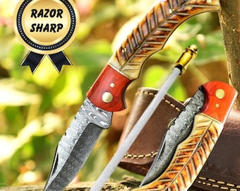 May include: A folding pocket knife with a Damascus steel blade, a red wood bolster, and a textured bone handle, accompanied by a sharpening rod and a brown leather sheath. A gold circular badge displays the text RAZOR SHARP.