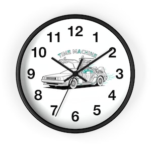 May include: A black-framed wall clock with a white face featuring black numerals and hands. The clock face includes a DeLorean car illustration with the words "TIME MACHINE" above it. The clock measures approximately 10 inches in diameter.