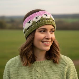 May include: A knitted headband with a sheep design. The headband has a pink top, white sheep, and a green base. The woman in the image is wearing a green sweater.
