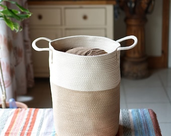 May include: A white and brown rope storage basket with two handles. The basket is filled with a brown ball of yarn.