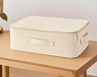 May include: A rectangular, off-white storage box with a zipper closure and two handles. The box is sitting on a wooden table. The box has a textured surface and is designed for organizing items.